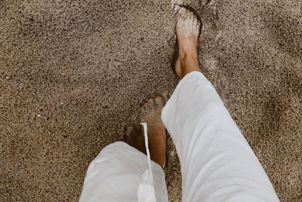 a close-up top view of two feet walking in the sand wearing white ankle length pants thinking i just want a peaceful life