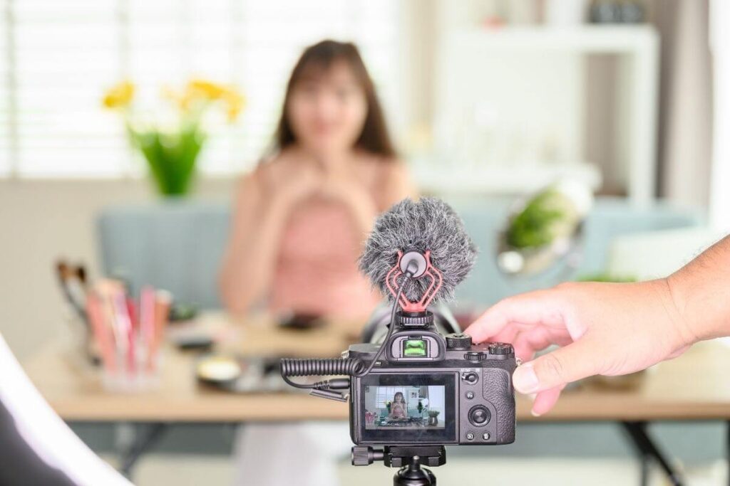 a blurred image of a female entrepreneur sitting at her well appointed simple desk recording a video promotion for her business with the back of the camera showing her image