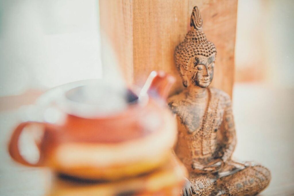 a photo of a buddha statute sitting against a wooden wall and a pot of tea sitting nearby