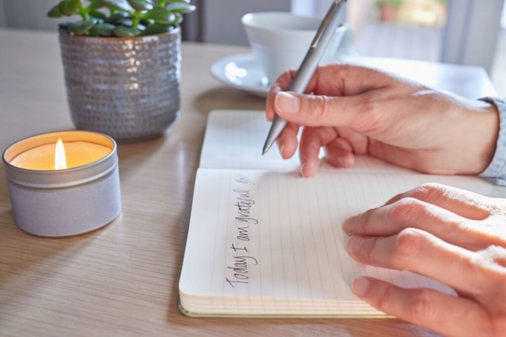 a top view of female hands writing in a journal with a small candle and potted succulent sitting in front of the journal