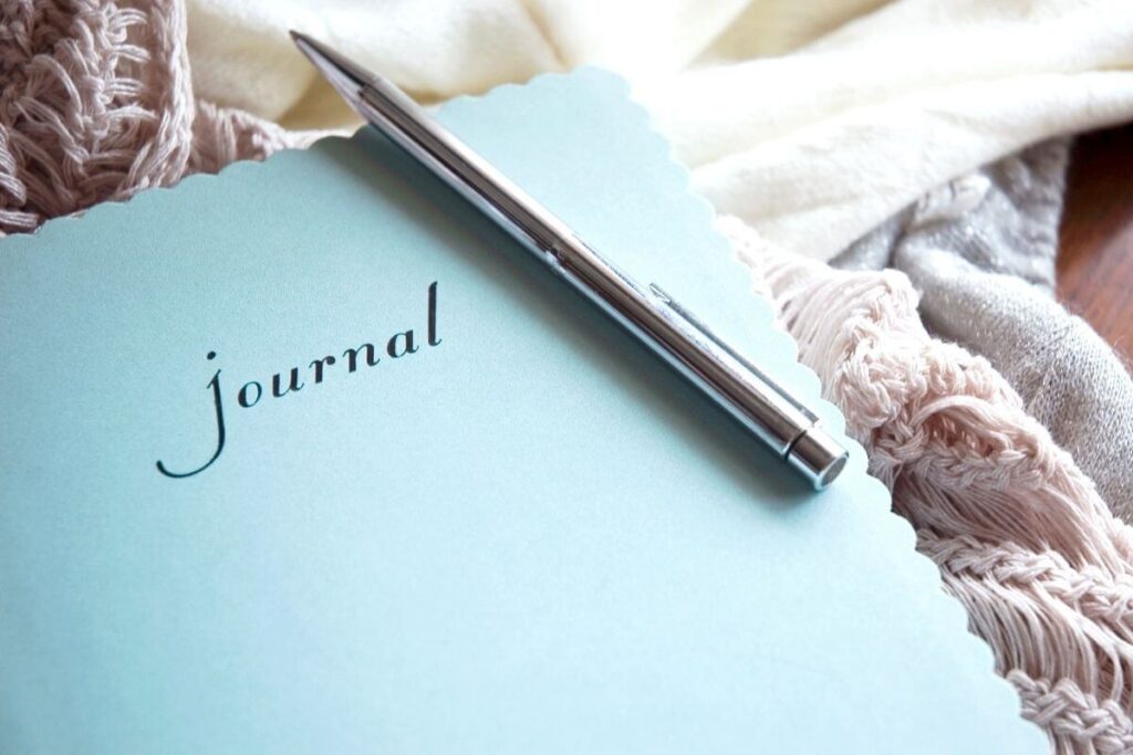 a top view of a journal and a pen sitting on a crocheted blanket as someone prepares to write about mindfulness journal prompts