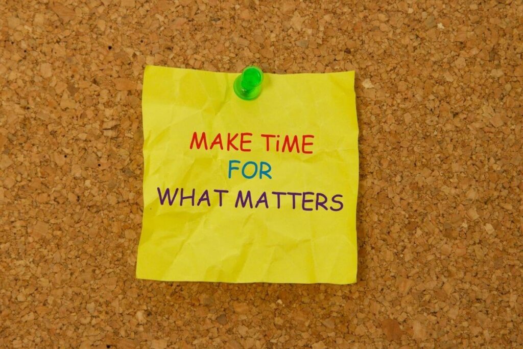 a bright yellow sticky note that says make time for what matters thumb tacked to a brown cork board