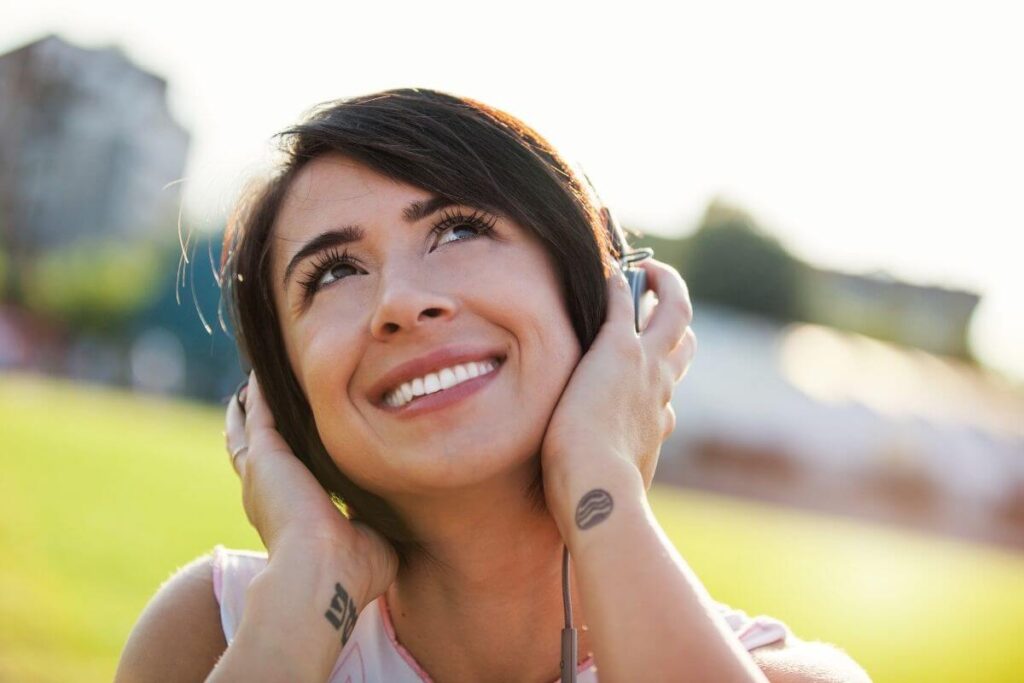 a woman uses personal growth tips to get outside in the sunshine and listen to music on her headphones to avoid career burnout