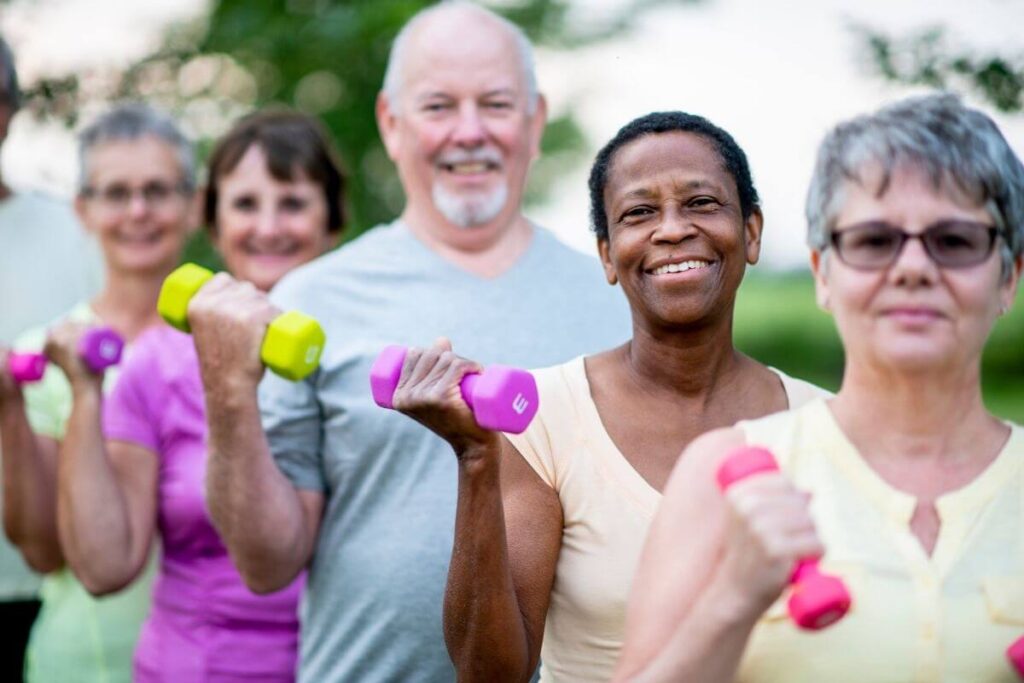 four middle aged women and a middle aged man exercise outside in a park using hand weights for personal growth and to avoid career burnout