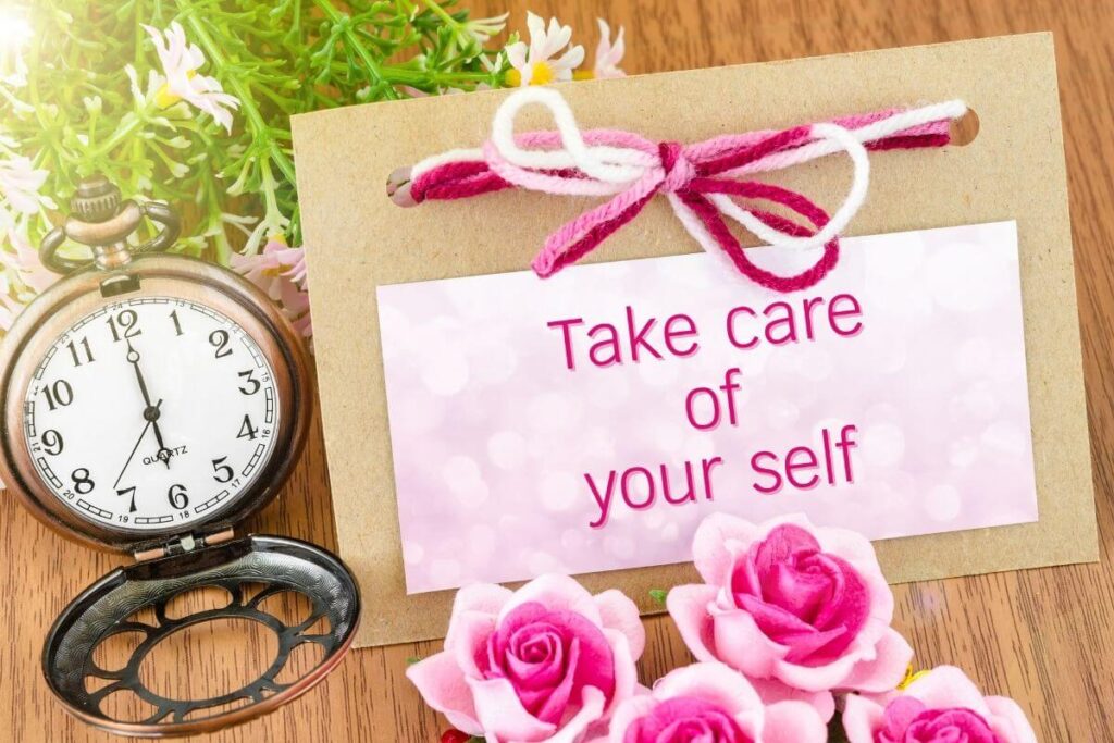 old fashioned clock and greenery and pink roses laying on a wooden table with a note that says take care of your self