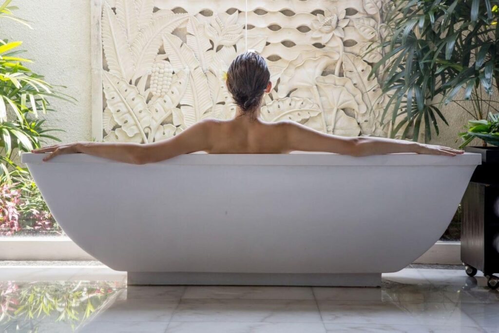 back view of a woman relaxing in a free standing bathtub with tree trees on each end of the tub