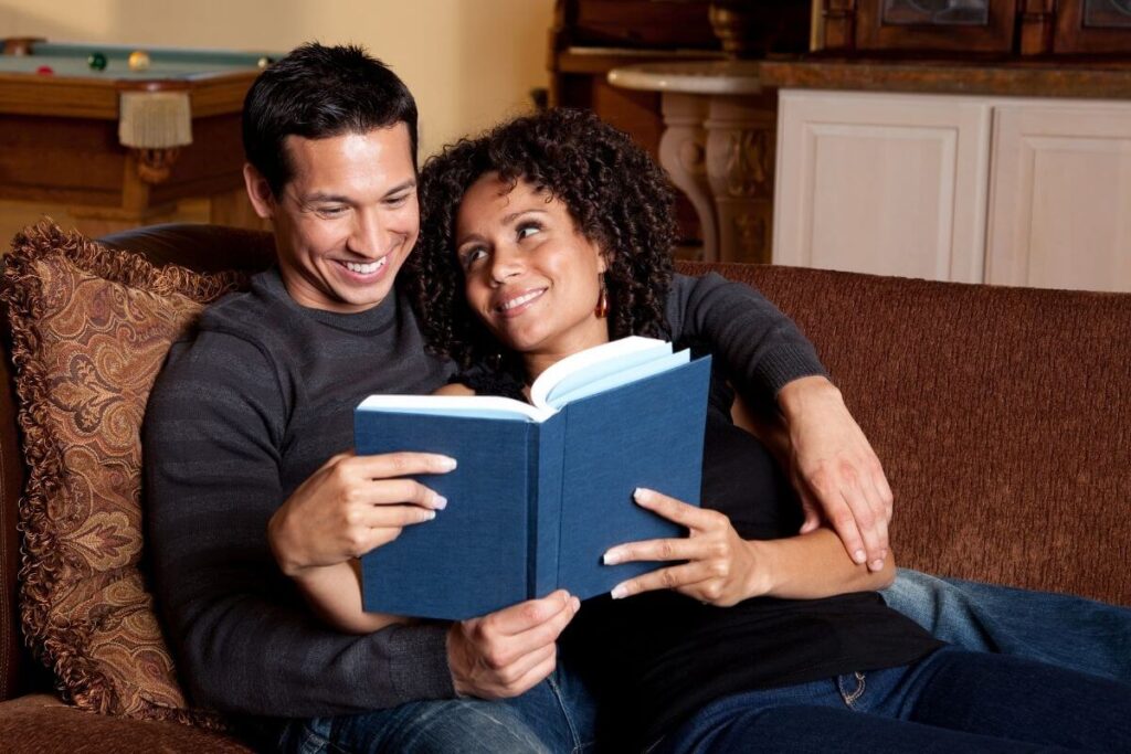 a happy couple relaxes on a sofa reading a book about top marriage problems and solutions because they want to be happier together