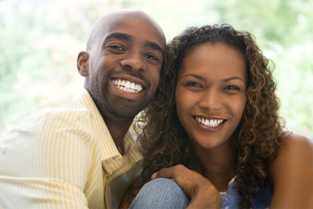 a happy couple smiles cheerfully at the camera as they sit close together in the park spending time together on a sunny day