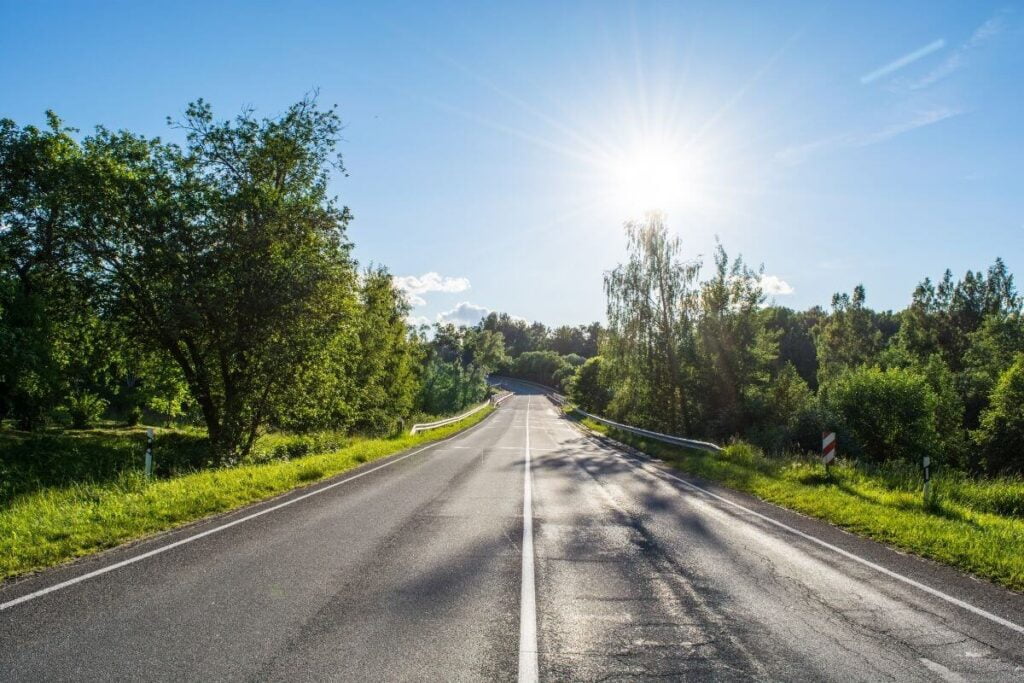 a long road ahead surrounded by trees and green grass with sunshine in the distance suggests that its time to let go of the past and move forward