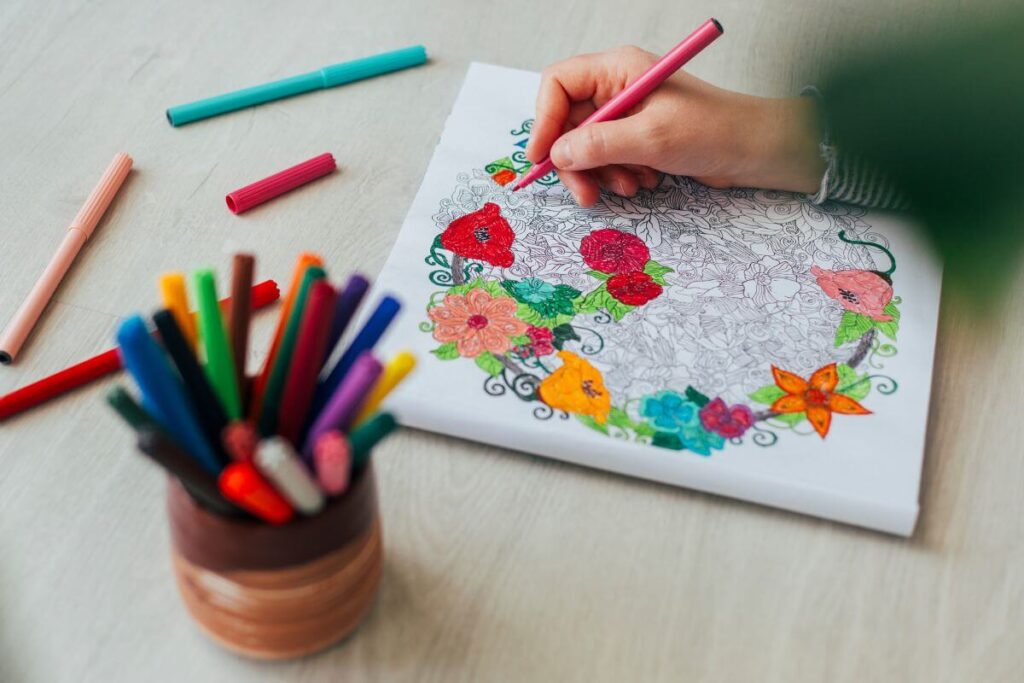 a top view of a female hand coloring in a book of adult coloring quotes and a cup of different colored pencils sitting next to her work