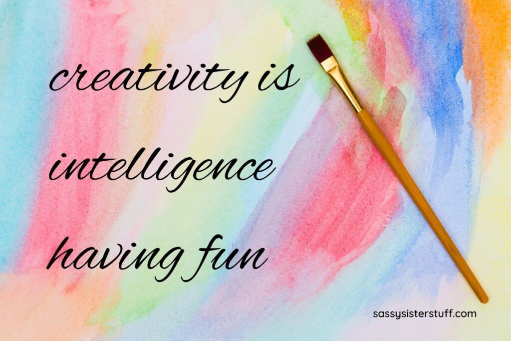 top view of a paint brush laying on sheet of paper that has been painted in soft rainbow colors and the quote creativity is intelligence having fun written on top