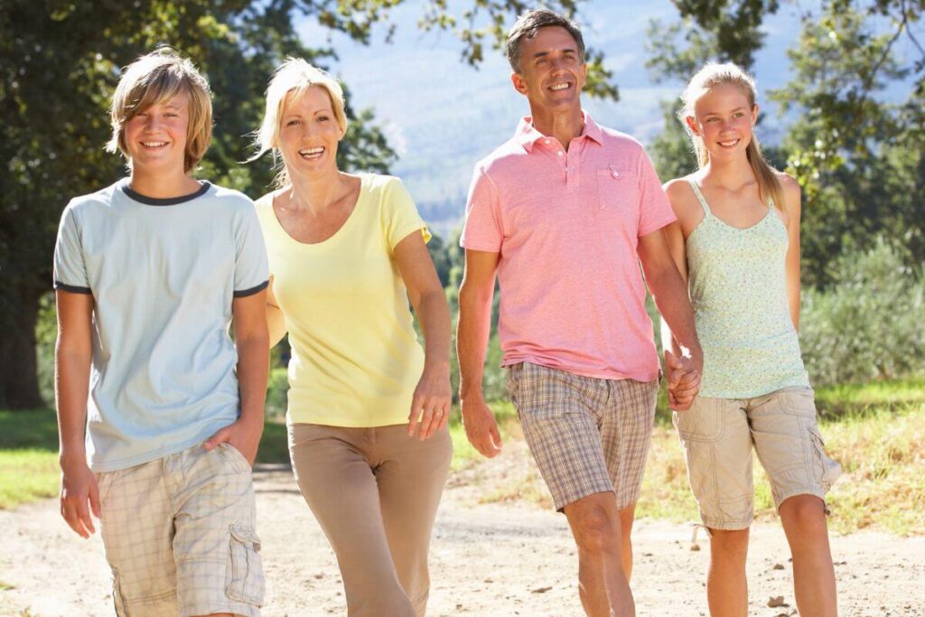 a family of four with a mom dad preteen boy and preteen girl walking on a path in a park because they believe it's important to fall in love with taking care of yourself