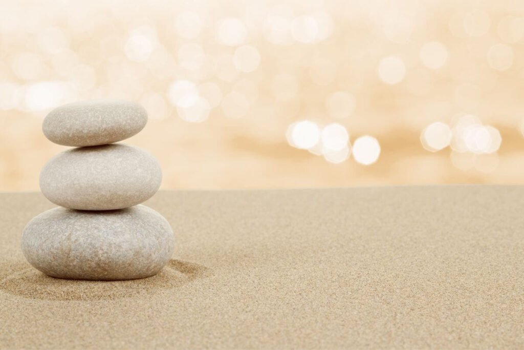 three tan stones stacked in the sand against a cream colored background showing great balance