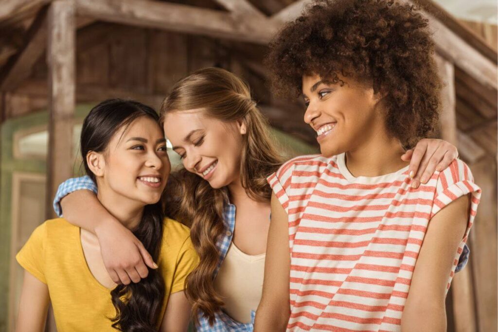 three beautiful young women joyfully embrace each other in a log cabin setting