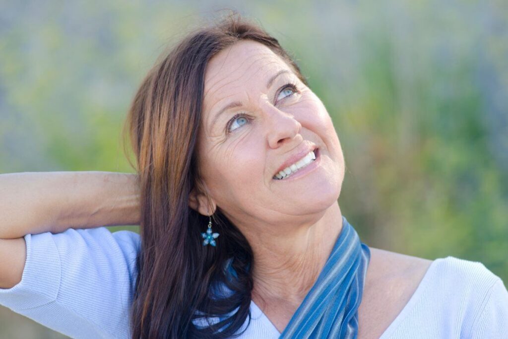 a middle aged woman cheerfully looks up to the sky because she feels happy after reading her monday affirmations