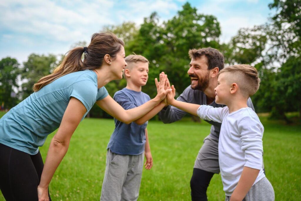 a mom dad and two boys excitedly give high fives together in a park