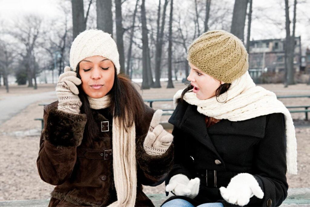 two women sit on a bench having a conversation about what is etiquette and why is it important while one rudely answers her phone to take a call