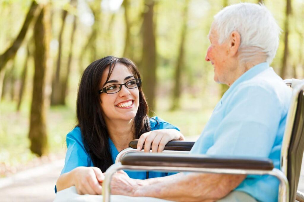 a young woman visits with a nursing home resident outside on a bright sunny day