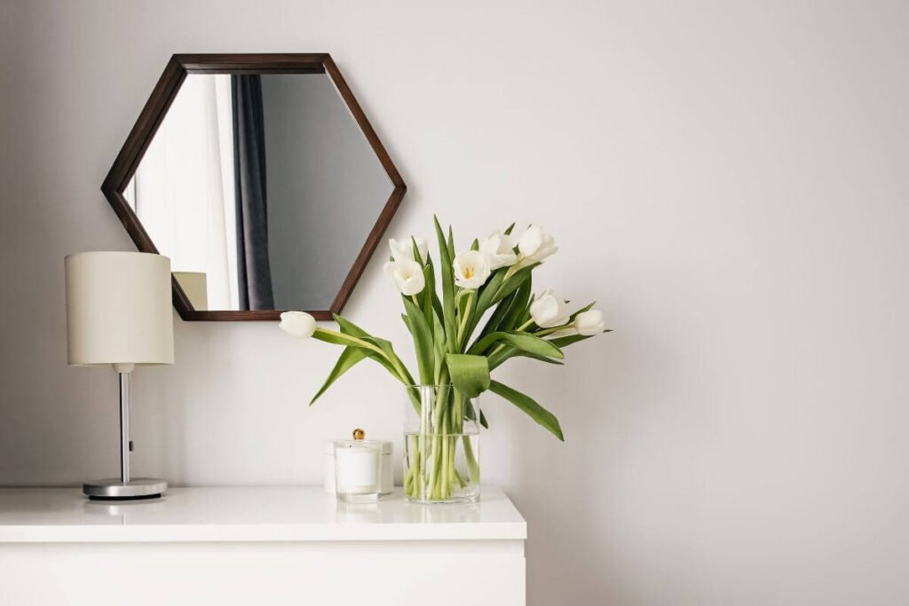 simple decor of flowers, candles, and a lamp on a bedroom dresser that sits under a mirror on the wall