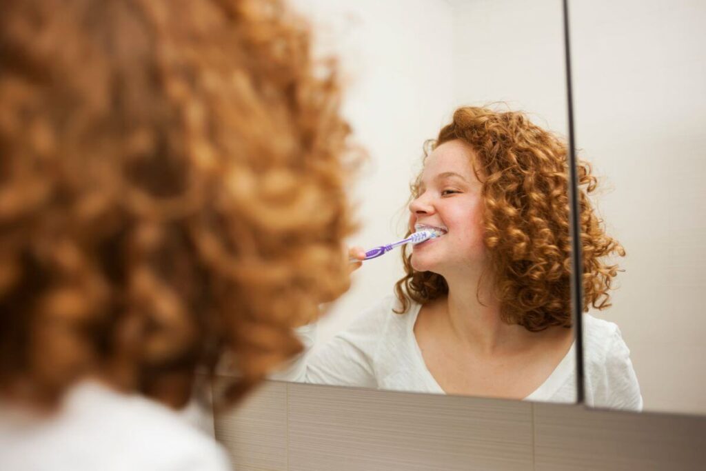 a happy red headed woman brushes her teeth before bedtime as part of her evening routing to make her life easier