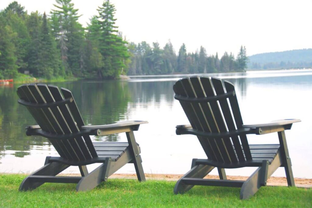 two wooden chairs sit on the shoreline of a peaceful lake