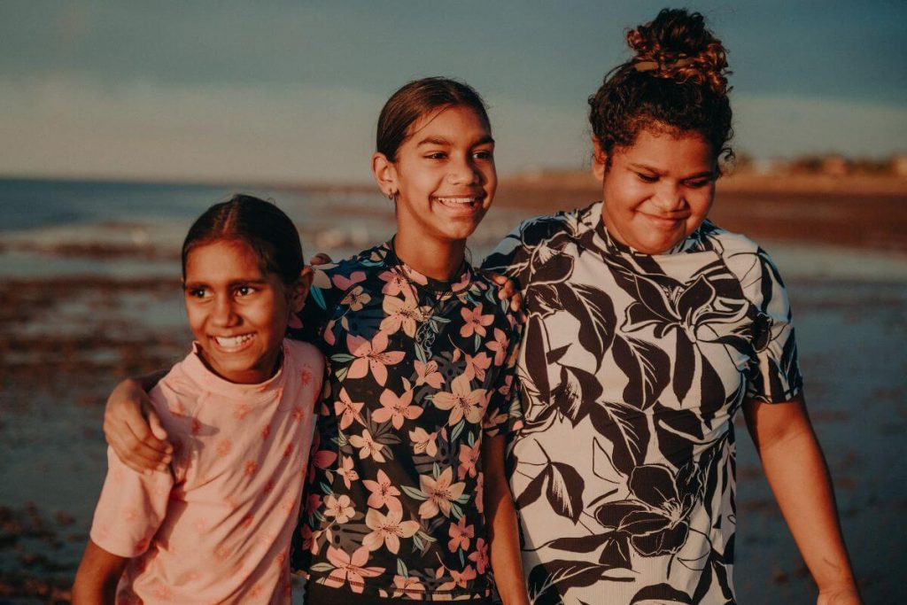 three young preteen girls with very different body types enjoy time strolling on the beach arm in arm