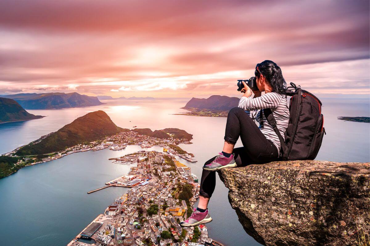 a young adventurous women taking photos sits on a large boulder over looking a city on the water