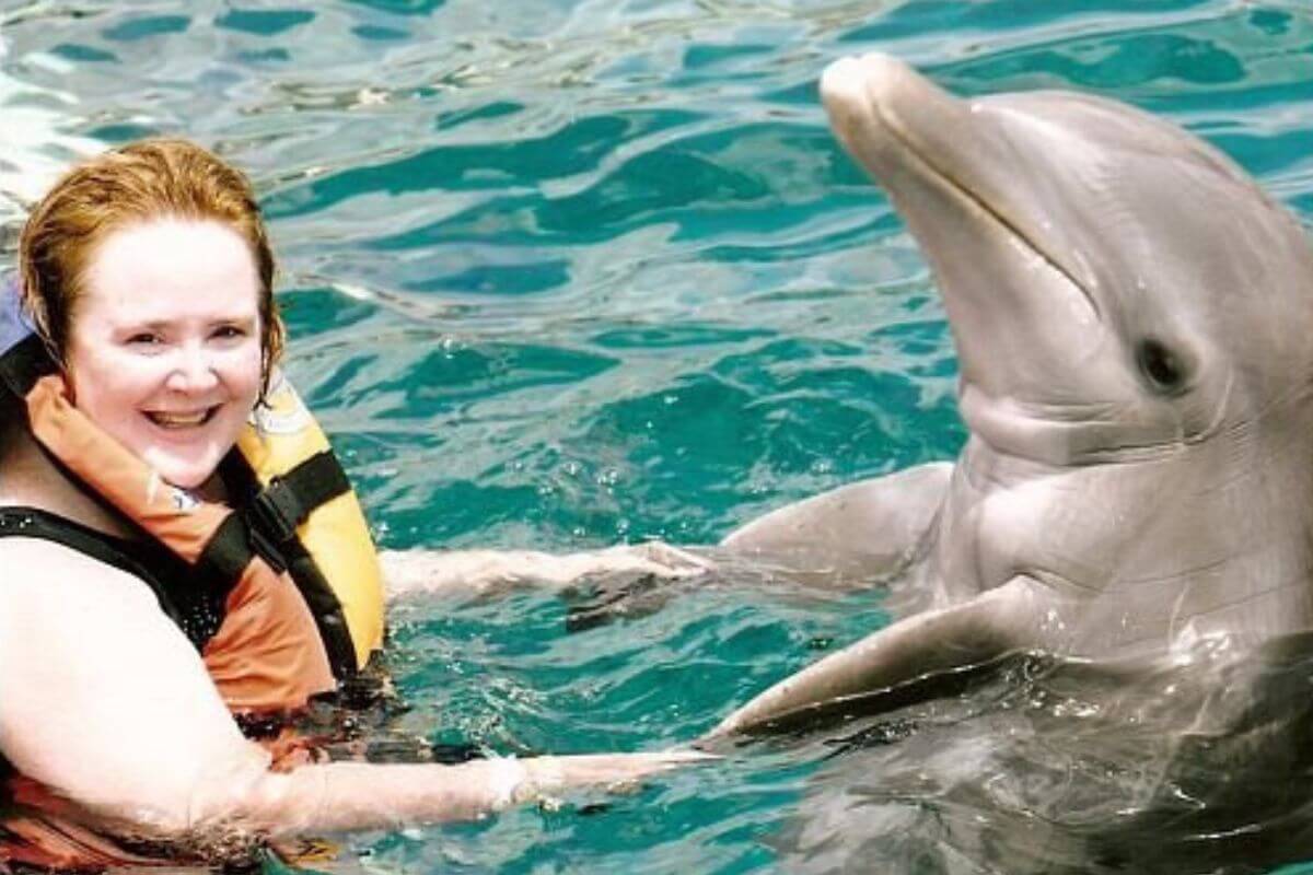 a middle aged woman poses with a dolphin in the crystal blue water