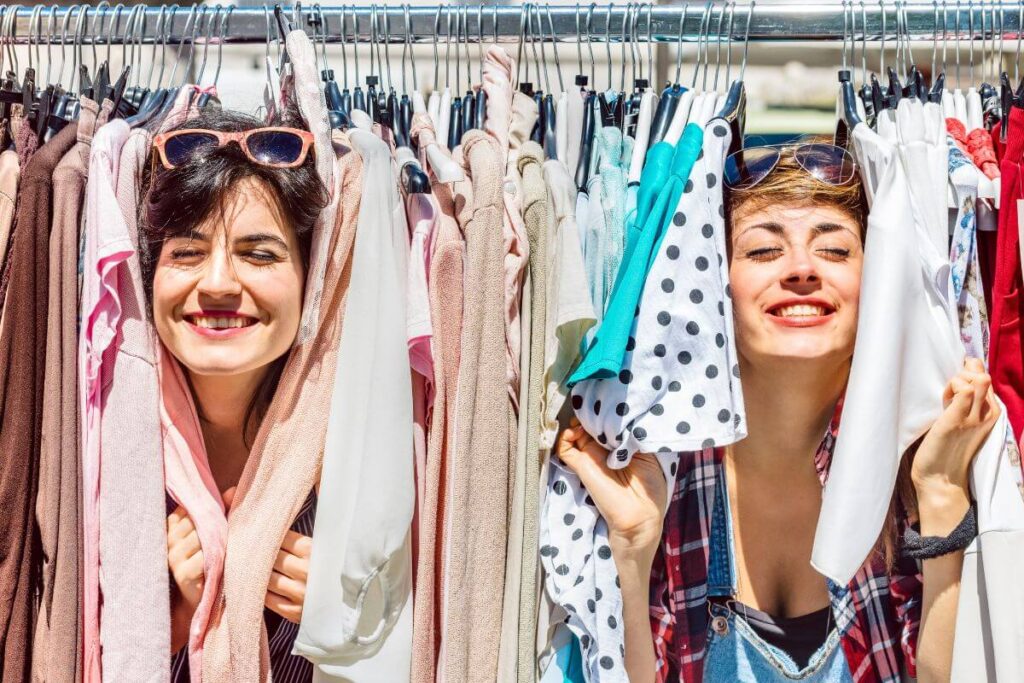 two laughing women make memories together being silly and peeking through a rack of clothes