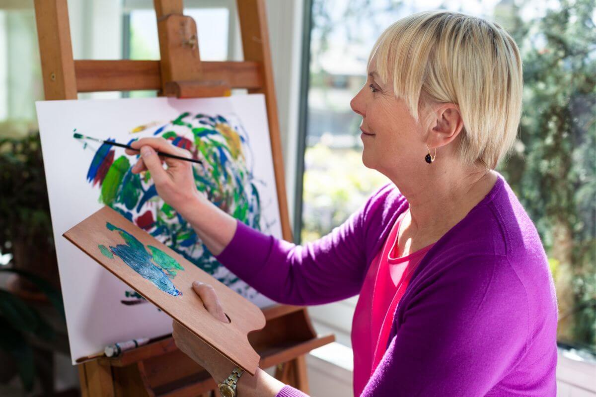 a middle aged woman paints on an easel in her home