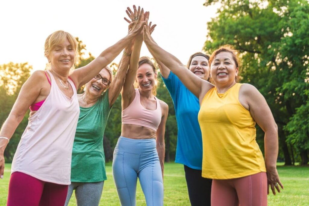 five middle aged sassy confident women high five after a yoga session outside in the park