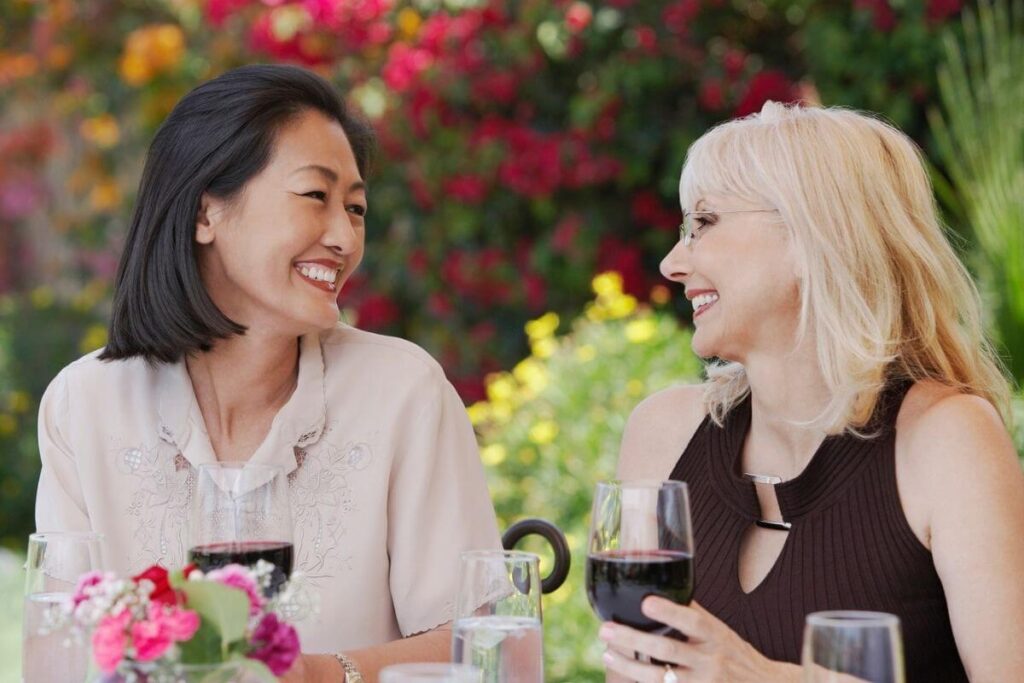 two middle aged women smile and enjoy a glass of wine together