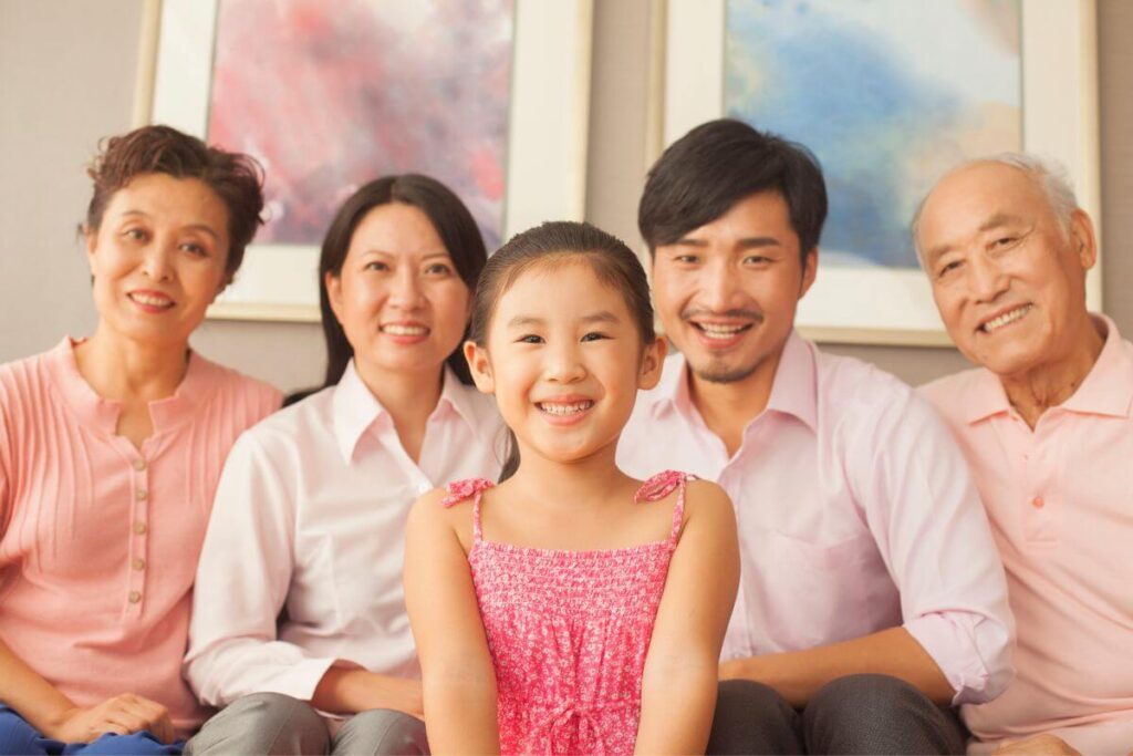 five members of a multigenerational Asian family sit together on a sofa