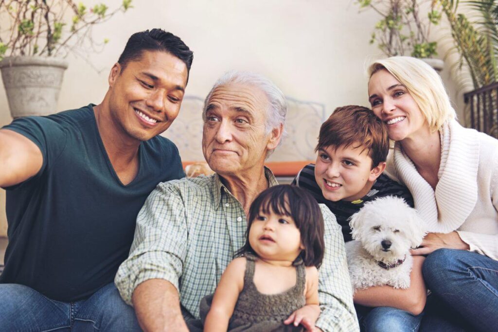 a young man takes a photo of his family that includes his elderly dad who lives with him and his wife and two children