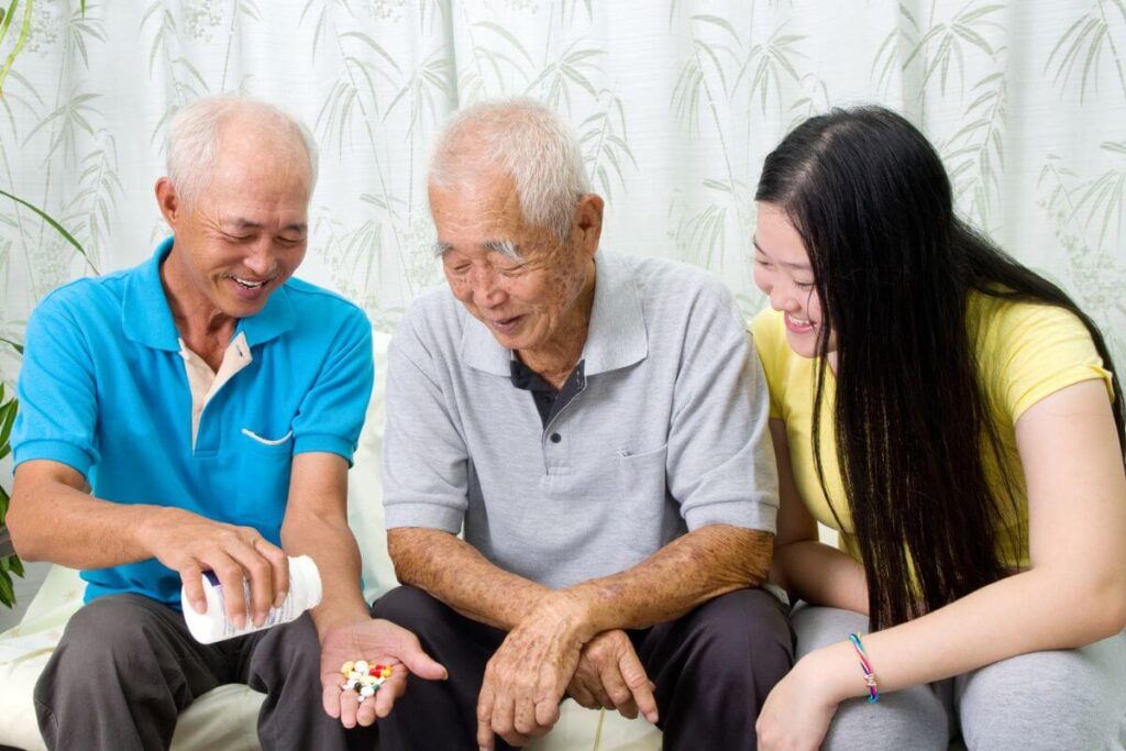 a young Asian couple lovingly helps their elderly father take his medications