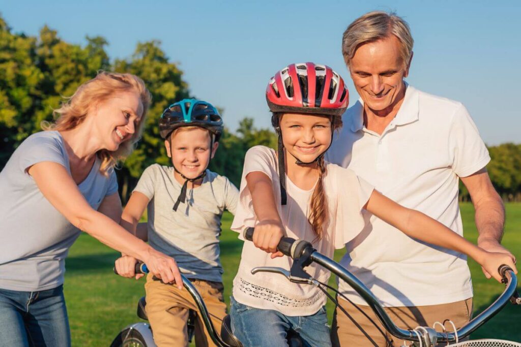 grandmother and grandfather help their grandchildren learn to ride a bike