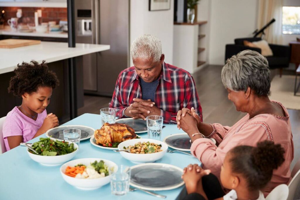 2 grandparents and 2 grandchildren lovingly gather at the dinner table to say grace before their meal together