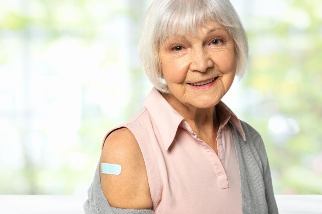 an elderly woman proudly shows the bandaid where she got her flu shot to keep her healthy and show that she cares about herself