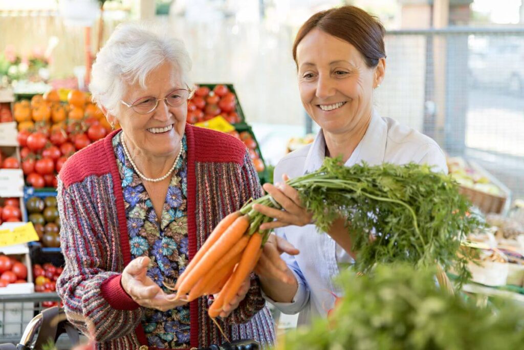 a middle aged woman and her elderly mother look at carrots while they do their grocery shopping together