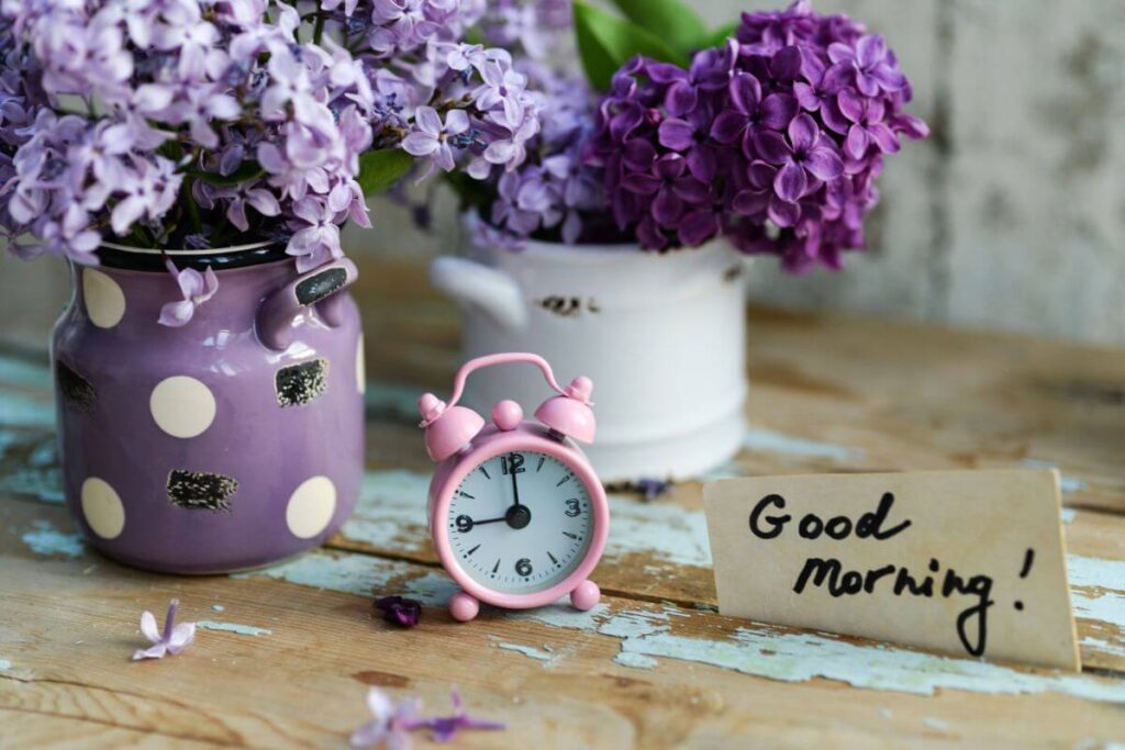 a close up of two jars of fresh lilacs, a small pink clock, and a small sign that says good morning! to help someone establish a healthy morning routine