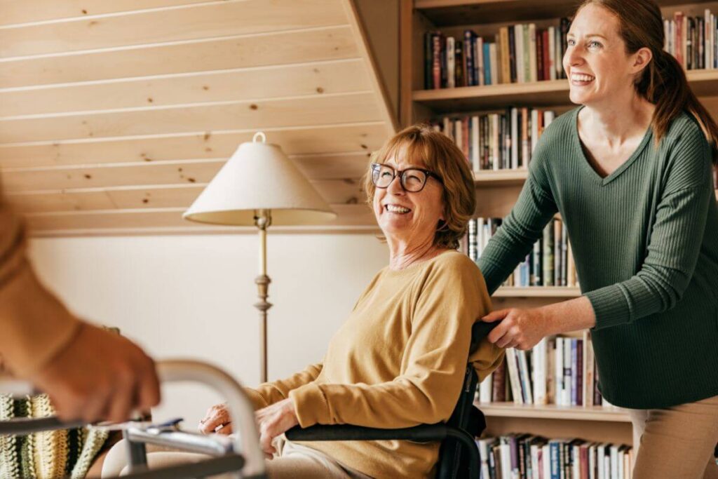 an adult daughter pushes her aging mother through a library in a wheelchair so she can access some social time with others