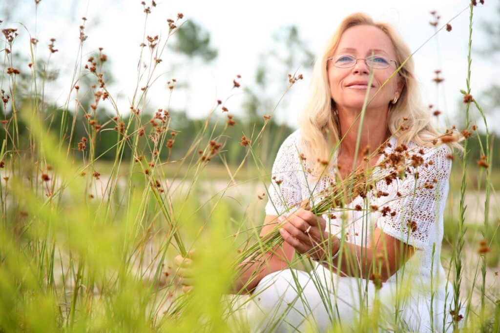 a middle aged woman sits among some wild flowers as she takes some time for self care while caring for her elderly parents