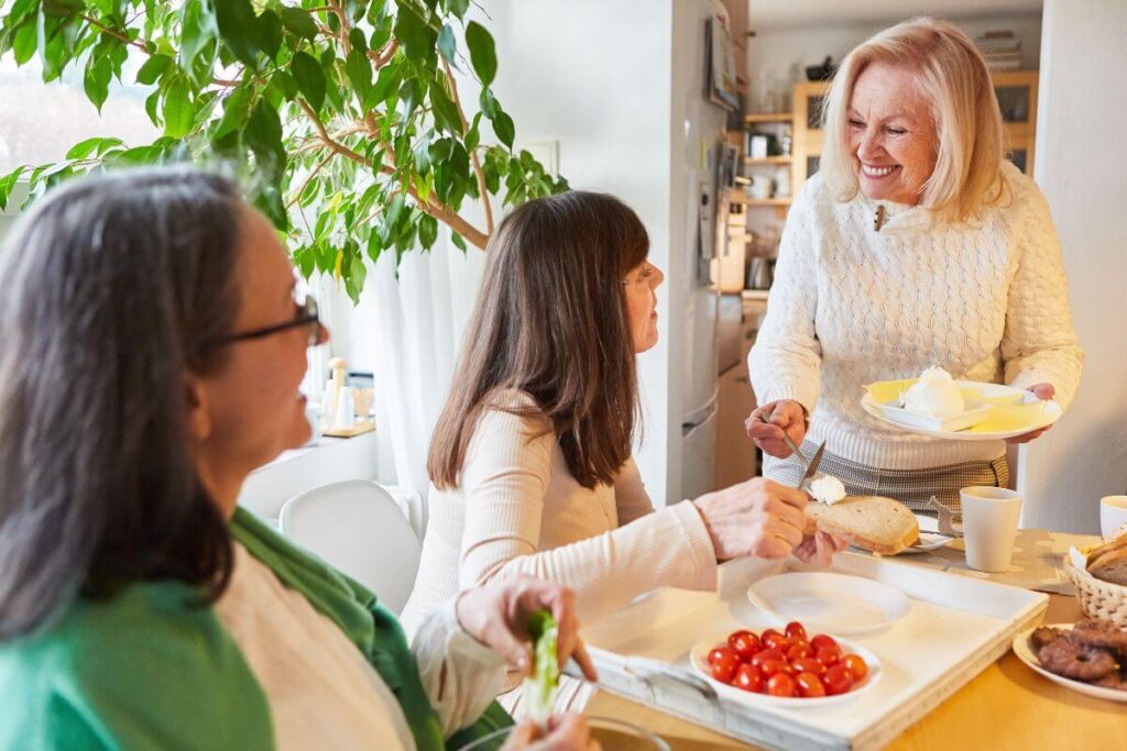 three happy middle aged women gather together in one of their homes to share a healthy lunch