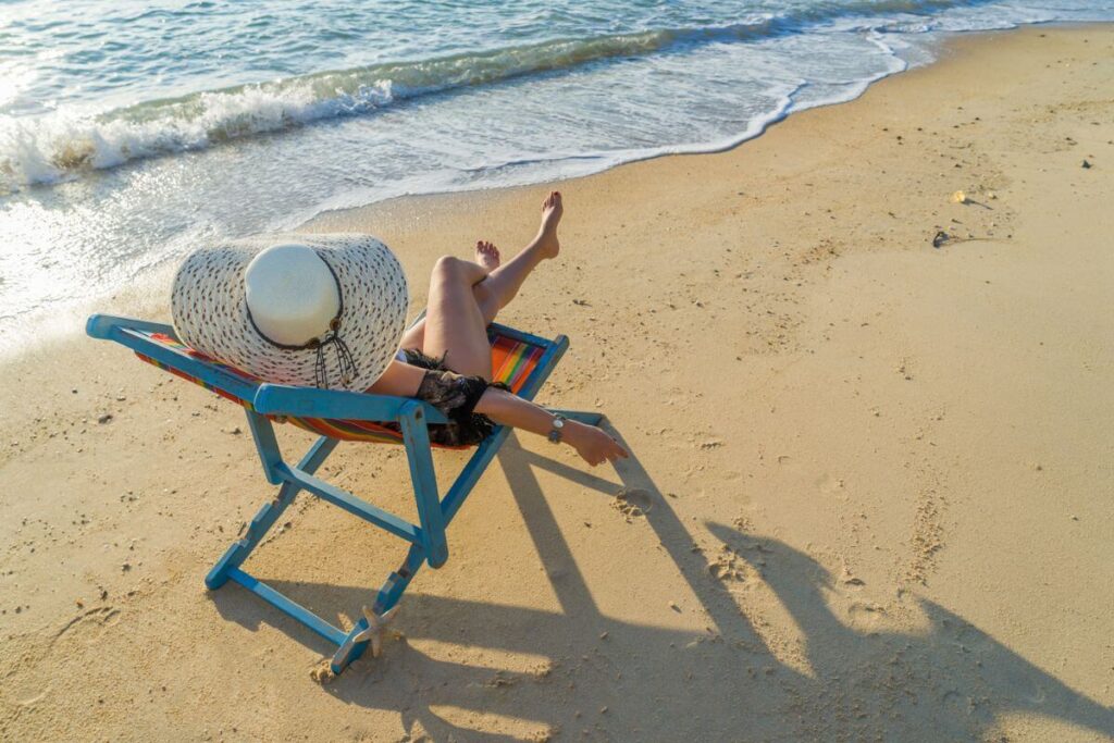 a woman sits happily in a chair along the shoreline because she is focusing on personal growth for women over 50 and she is learning to relax