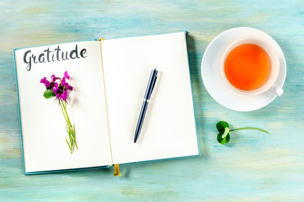 a top view of a gratitude journal with a pen laying on it and a cup of tea next to it