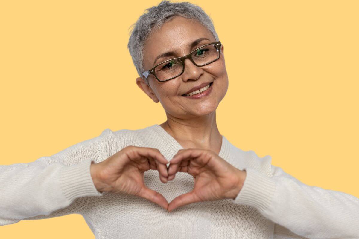 a beautiful middle-aged women smiles and makes a heart with her hands to show an attitude of gratitude