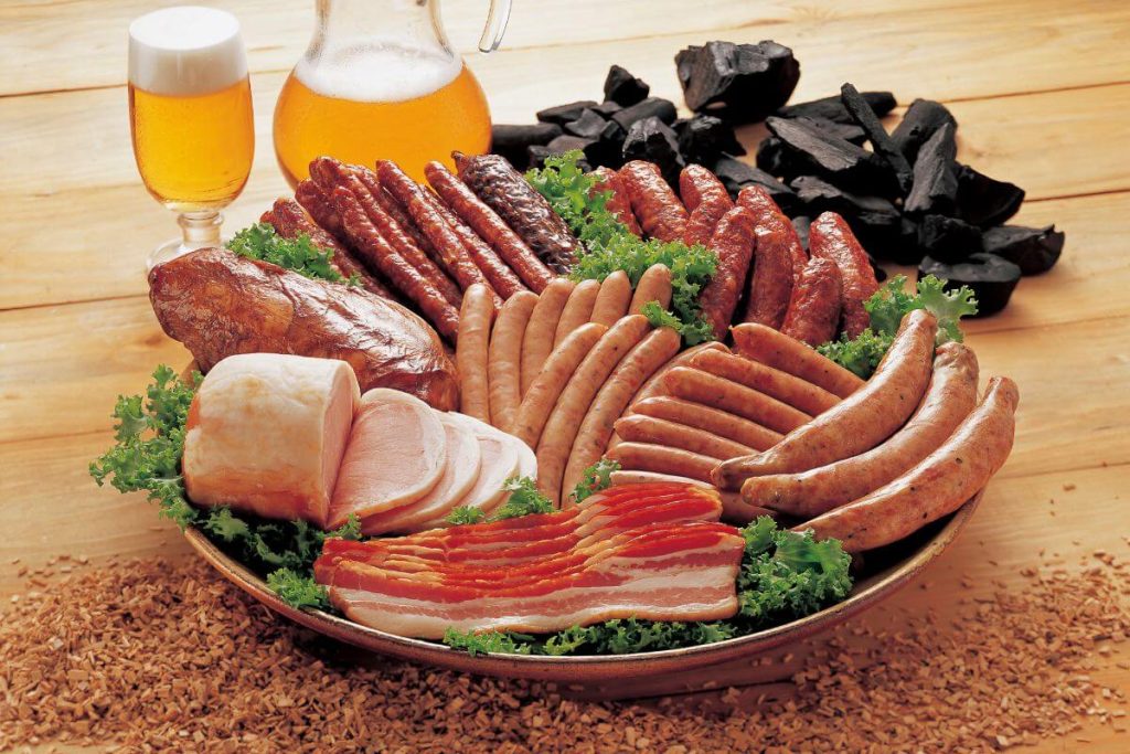 a plate of processed meat, a pitcher of beer, and a pile of chocolate show many foods to avoid after turning 60