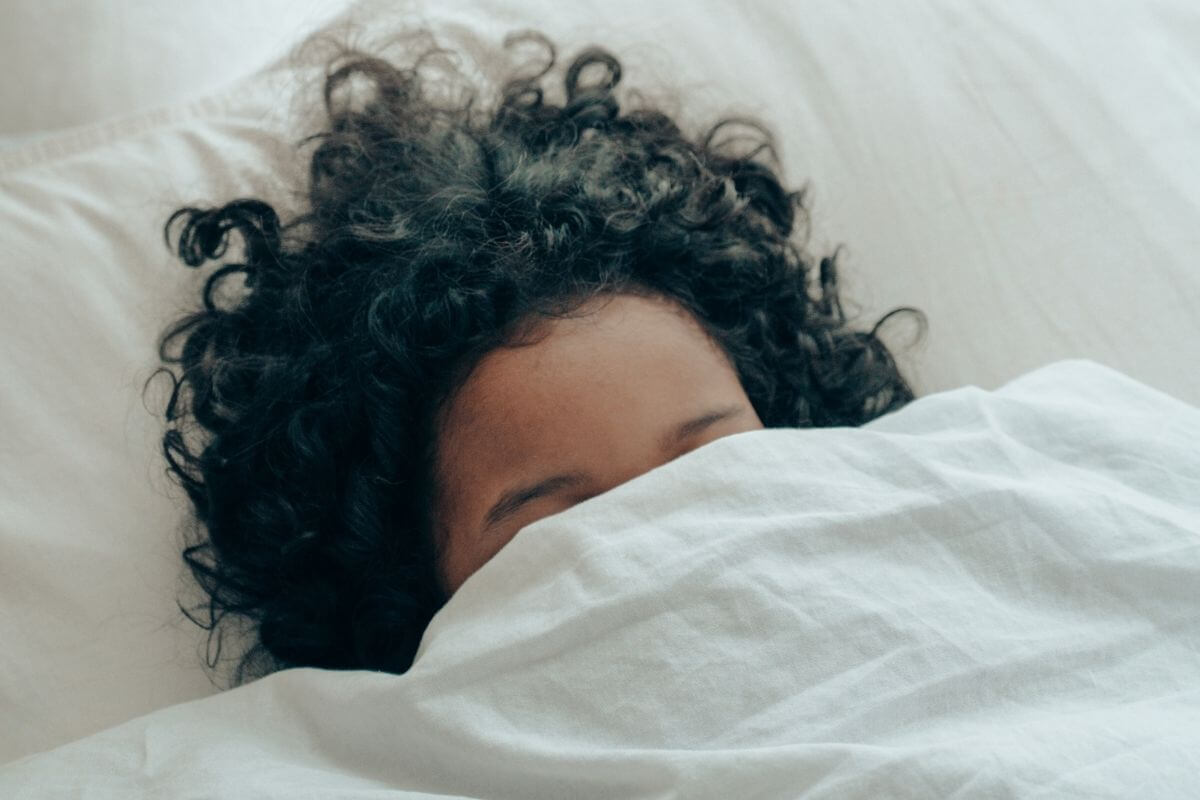 a black female peeks out from under her bed sheets because she doesn't know how to make friends with social anxiety