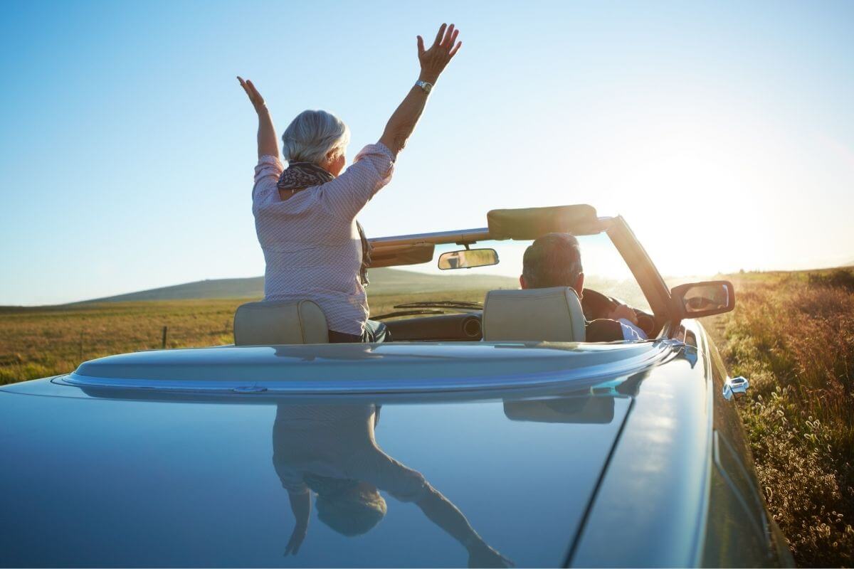 middle aged couple in a convertible looking out over the sunset together