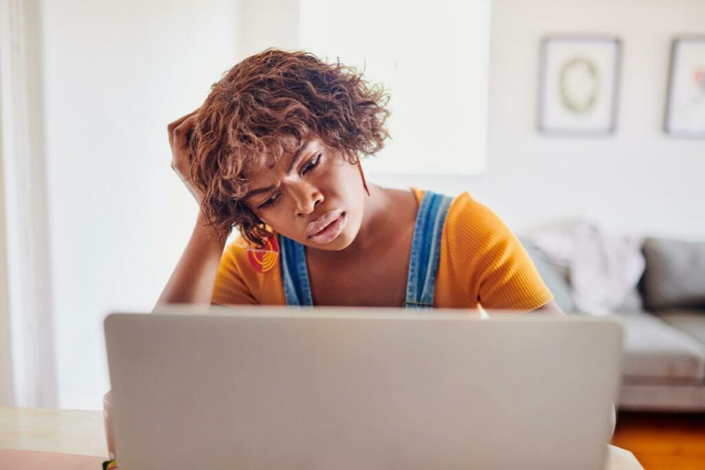 frustrated black woman sits at a lap top with her head resting on her hand wondering why is life so hard